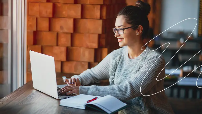 Fotografía de una mujer con gafas realizando tareas de contabilidad y finanzas en su escritorio con computadora enfrente y una calculadora al lado. 