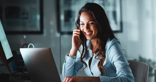 Una mujer profesional usa teléfono mientras mira su computadora portátil.