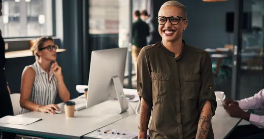 Un joven sonriente con gafas de pie frente a un grupo de personas en un centro de cómputo