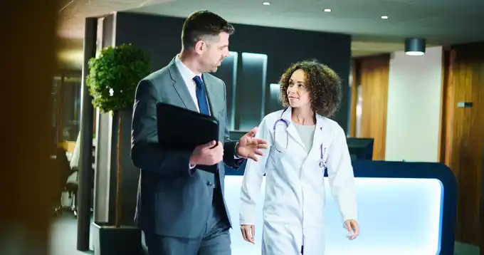 Un hombre y una mujer en bata de médico conversar en un pasillo de hospital