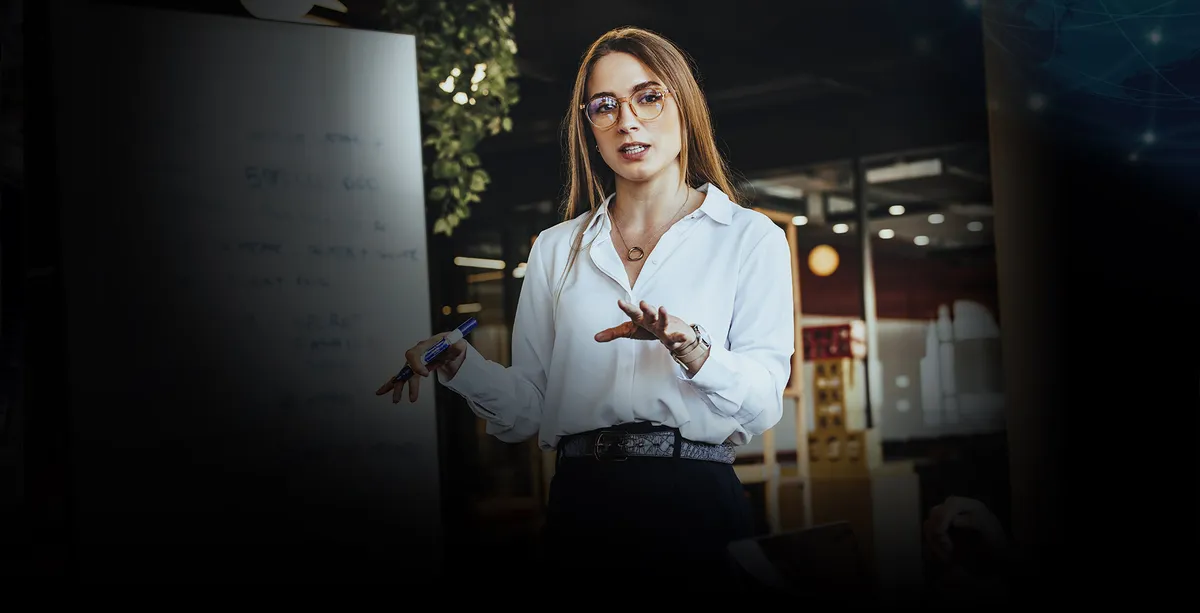 Mujer experta en planeación estratégica educativa explica frente a pizarra.