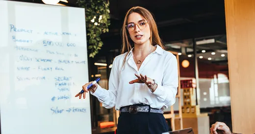 Mujer experta en planeación estratégica educativa explica frente a pizarra.