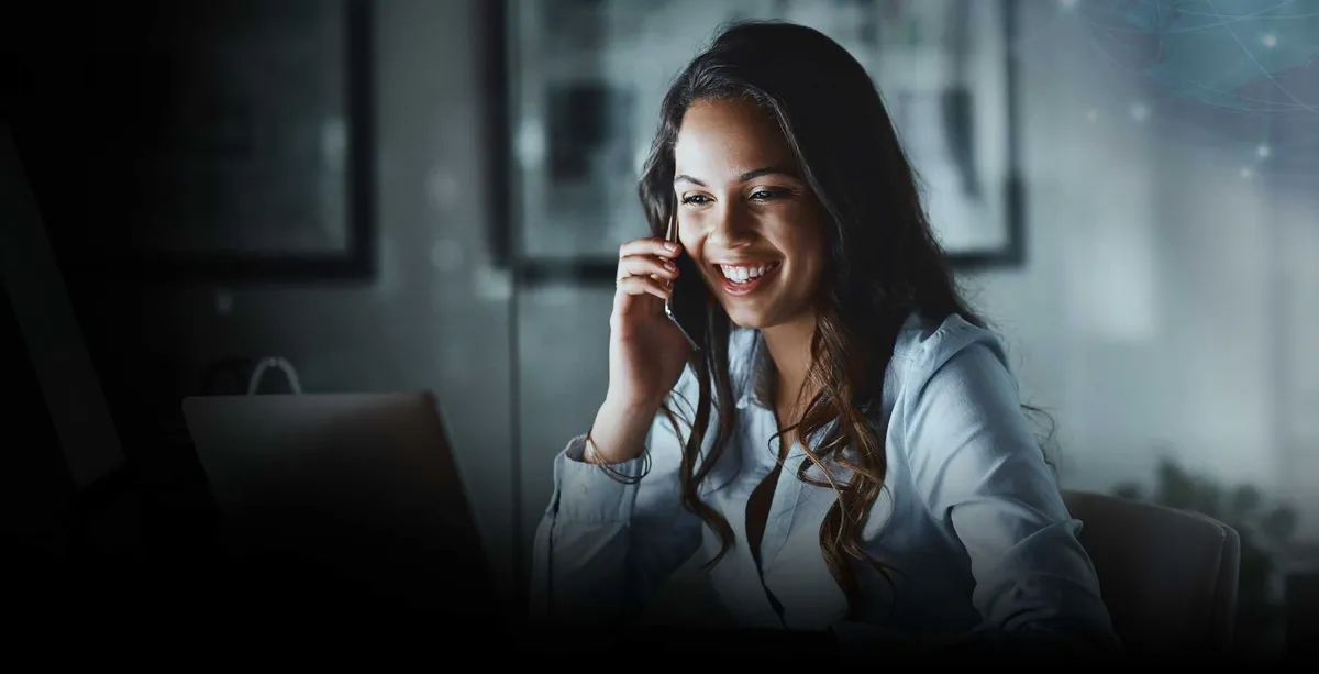 Una mujer profesional usa teléfono mientras mira su computadora portátil.