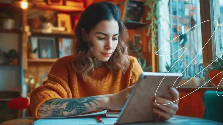 Una mujer joven sonriente tomando una clase de negocios a través de una tablet en una cafetería. 